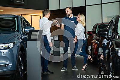 The seller hands over the car keys to the buyers. The couple bought a new car. Stock Photo