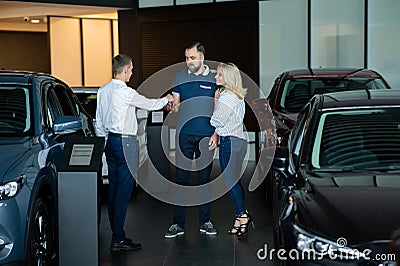 The seller hands over the car keys to the buyers. The couple bought a new car. Stock Photo