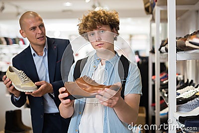 Seller offers various shoes to a teenager in shoe store Stock Photo