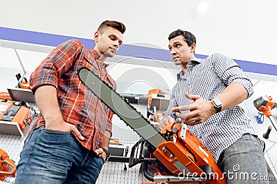 The seller in the store shows the customers a chainsaw. Stock Photo