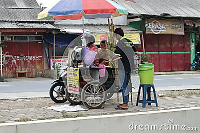 a seller of sugar cane juice drinks serving a customer on the side of the main road close to the city park Editorial Stock Photo