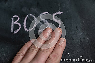 The semi-erased word BOSS on the black chalkboard. An adult man`s left hand removes the handwritten word with his fingers. Fuzzy Stock Photo