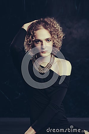 A semi-profile portrait of transgender guy model with blue eyes and blond hair in the image of a girl with chain around neck Stock Photo