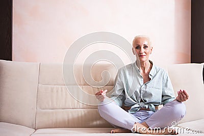 Senior Adults and Yoga Concepts. Portrait of Relaxing Caucasian Senior Woman Posing in Yoga Asana Pose on Couch indoors. Sitting Stock Photo