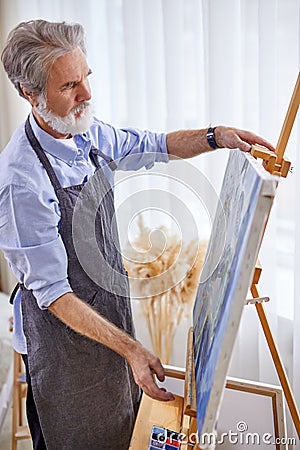 gray bearded artist painting on easel, canvas Stock Photo