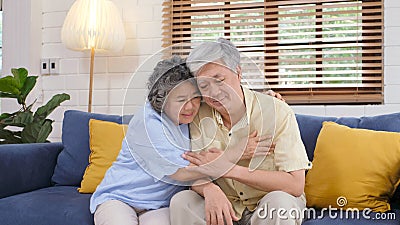 Senior asian couple comforting each other from depressed emotion while sitting on sofa at home living room, old retirement Stock Photo