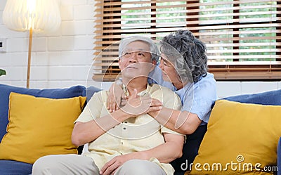 Senior asian couple comforting each other from depressed emotion while sitting on sofa at home living room, old retirement Stock Photo