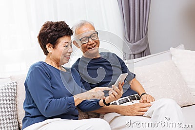 Senior Asian couple grandparents using a smart phone together on sofa at home. Stock Photo