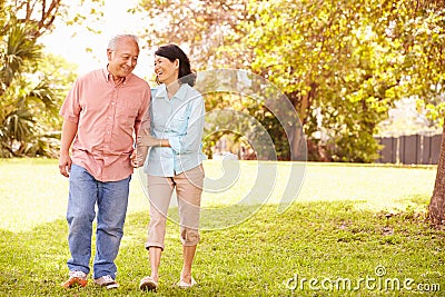 Senior Asian Couple Walking Through Park Together Stock Photo