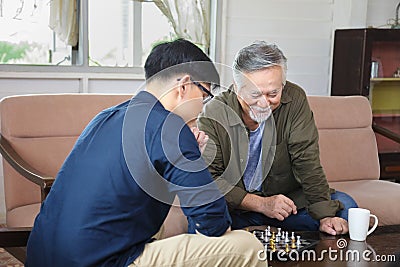Senior Asian man playing chess with his son in the living room for elder and family concept Stock Photo