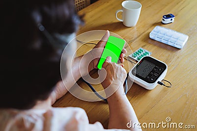 Senior asian woman is measuring blood pressure and heart rate with digital pressure gauge electric tonometer by herself at home Stock Photo