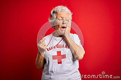 Senior beautiful grey-haired lifeguard woman wearing t-shirt with red cross using whistle Yawning tired covering half face, eye Editorial Stock Photo