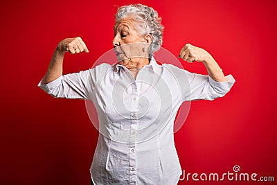 Senior beautiful woman wearing elegant shirt standing over isolated red background showing arms muscles smiling proud Stock Photo