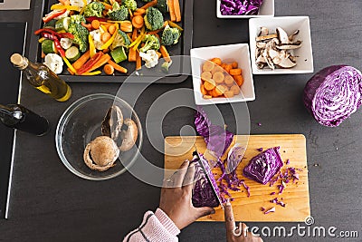 Senior biracial woman with prepared vegetables in bowls on table cutting cabbage in kitchen at home Stock Photo