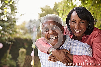 Senior black couple piggyback in garden looking at camera Stock Photo