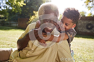 Senior black man sitting on grass, embraced by his grandson Stock Photo