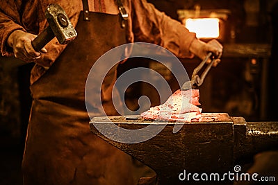 Senior blacksmith forging the molten metal on the anvil in smithy Stock Photo