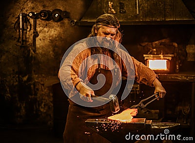 Senior blacksmith forging the molten metal on the anvil in smithy Stock Photo