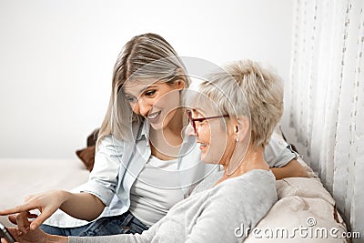 A senior blonde woman has a tablet in her hand while a young woman explains how to use the internet,iptv, social networks and Stock Photo
