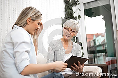 A senior blonde woman has a tablet in her hand while a young woman explains how to use the internet, social networks and online Stock Photo