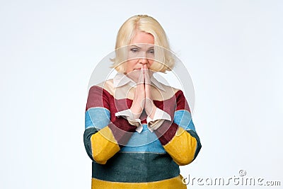 Senior blonde woman pressing palms together, having mournful facial expression Stock Photo