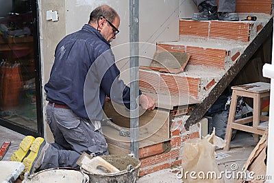 Senior bricklayer building a ceramic wood effect staircase in a home. Stock Photo