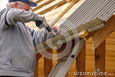 Senior builder man with a screwdriver screwing a roofing sheet to the roof Stock Photo