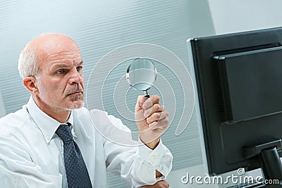 Senior businessman examines computer, magnifying precision Stock Photo