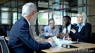 Senior businessman looking at colleagues arguing and shouting, stressful work Stock Photo