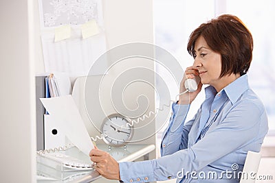 Senior businesswoman on phone call reading paper. Stock Photo