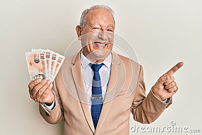 Senior caucasian man holding united kingdom pounds smiling happy pointing with hand and finger to the side Editorial Stock Photo