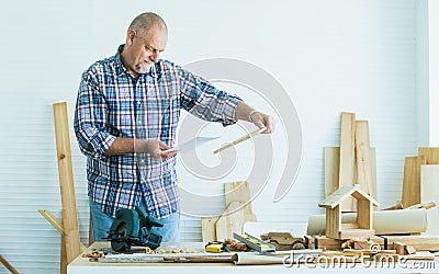 Senior Caucasian retired old male woodworker, carpenter reading, rechecking and comparing drawing plan with finish wooden figure Stock Photo