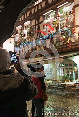 Senior citizen taking a photo with cell phone of beautifully decorated half-timbered houses in La Petite France in historic Editorial Stock Photo