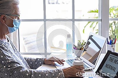 Senior concentrated woman working on laptop from home wearing surgical mask due to covid-19, active modern social and Stock Photo