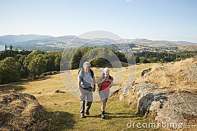 Senior Couple Climbing Hill On Hike Through Countryside In Lake District UK Together Stock Photo