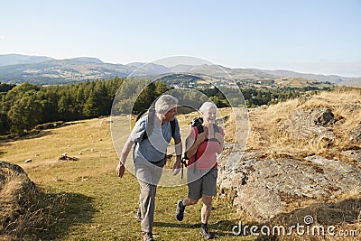 Senior Couple Climbing Hill On Hike Through Countryside In Lake District UK Together Stock Photo