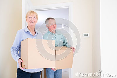 Senior Couple Downsizing In Retirement Carrying Boxes Into New Home On Moving Day Stock Photo