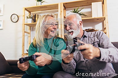 Senior couple having fun at home playing video game holding joysticks in hands. Stock Photo