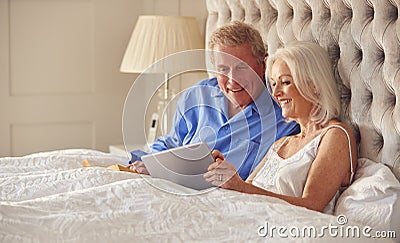 Senior Couple At Home In Bed Self Isolating Using Digital Tablet During Covid 19 Lockdown Stock Photo