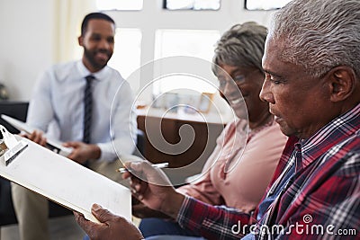 Senior Couple Meeting With Male Financial Advisor At Home And Signing Document Stock Photo