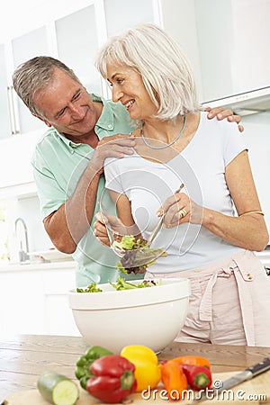 Senior Couple Preparing Salad In Modern Kitchen Stock Photo
