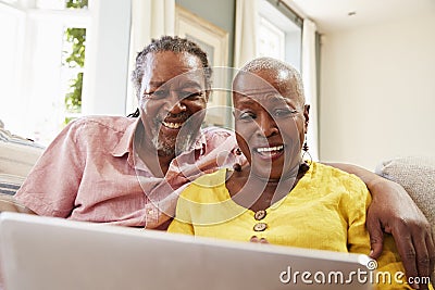 Senior Couple Sitting On Sofa Using Laptop At Home Together Stock Photo