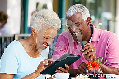 Senior Couple Using Tablet At Outdoor Cafe Stock Photo