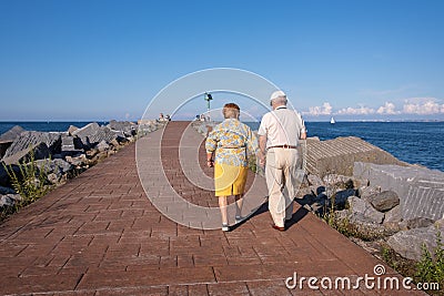 Senior couple walking by the sea. Aged people with a healthy lifestyle. Long lasting couple holding hands. Life expectancy is high Editorial Stock Photo