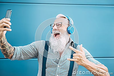 Senior crazy man taking self video while listening music with headphones - Hipster guy having fun using mobile smartphone Stock Photo