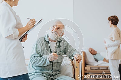 Senior doctor in a beige uniform talks to an elderly patient during a walk around hospital Stock Photo