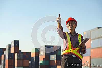 A senior elderly Asian worker engineer wearing safety vest and helmet standing and holding digital tablet at shipping cargo Stock Photo