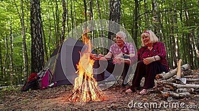 Senior elderly grandmother grandfather cooking frying sausages over campfire in wood at camping Stock Photo