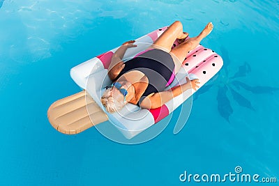 Senior female woman with bright sun glasses lies on a swimming pool inflatable icecream shaped float Stock Photo