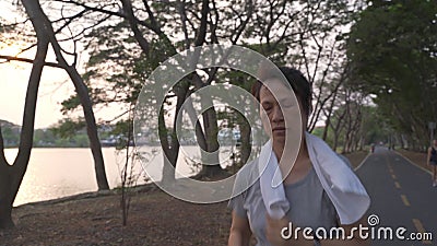 Senior femme athlète asiatique avec casque sans fil courant dans le parc des arbres de la ville pendant le coucher du soleil du so clips vidéos Senior femme athlète asiatique avec casque sans fil courant dans le parc des arbres de la ville pendant le coucher du soleil du so clips vidéos